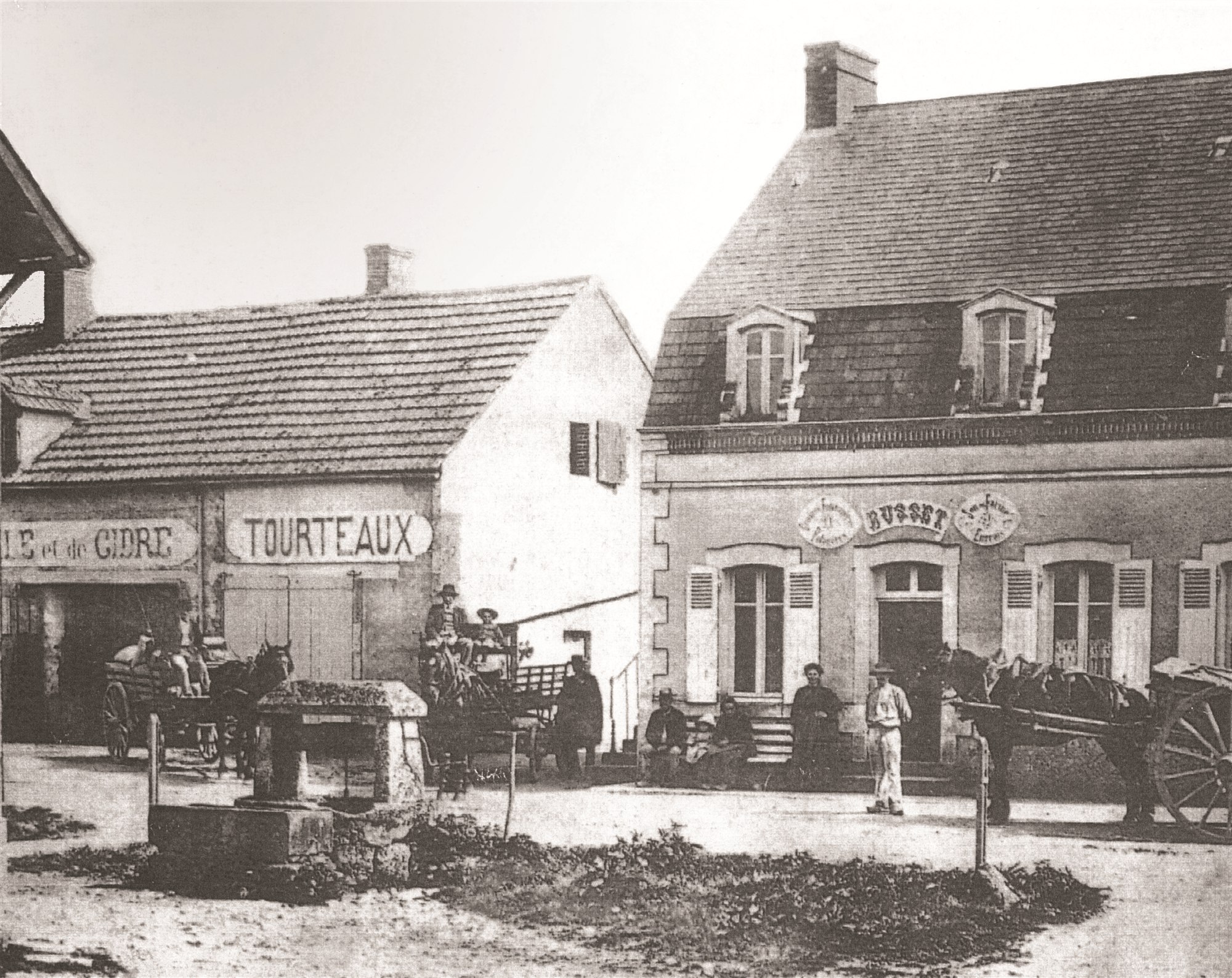 La maison de la famille Busset à Boucé, photographiée en 1910, avec des habitants et des attelages devant la façade